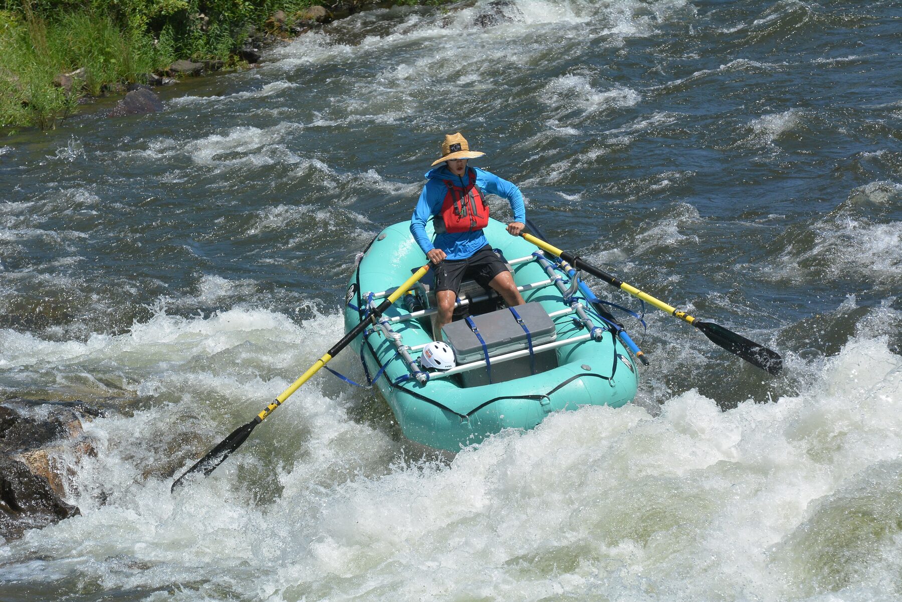 The teal 10.5-foot RMR raft running a rapid